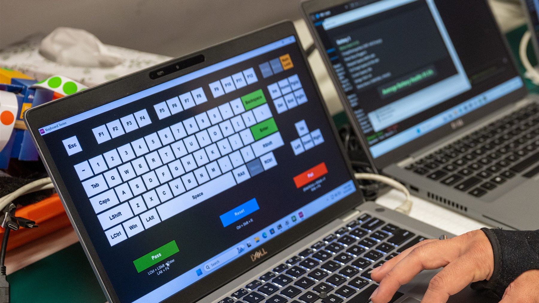 A laptop displaying a keyboard test while a technician presses its keys.