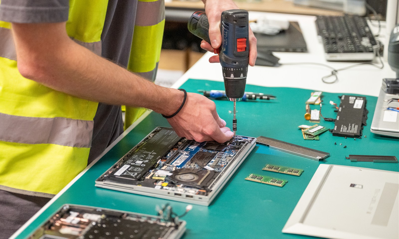 A technician working on an opened laptop at a green workshop bench.