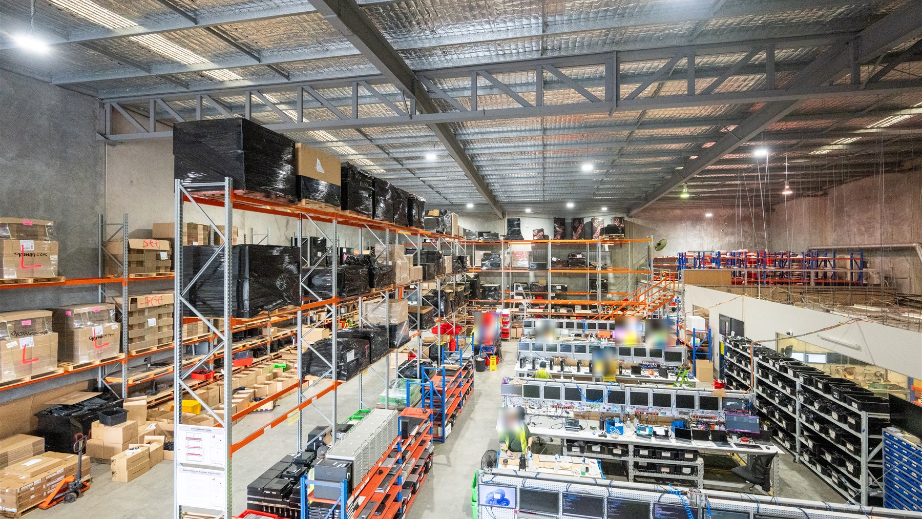 Warehouse racking and rows of computer workbenches inside ACT's warehouse, with staff faces obscured.