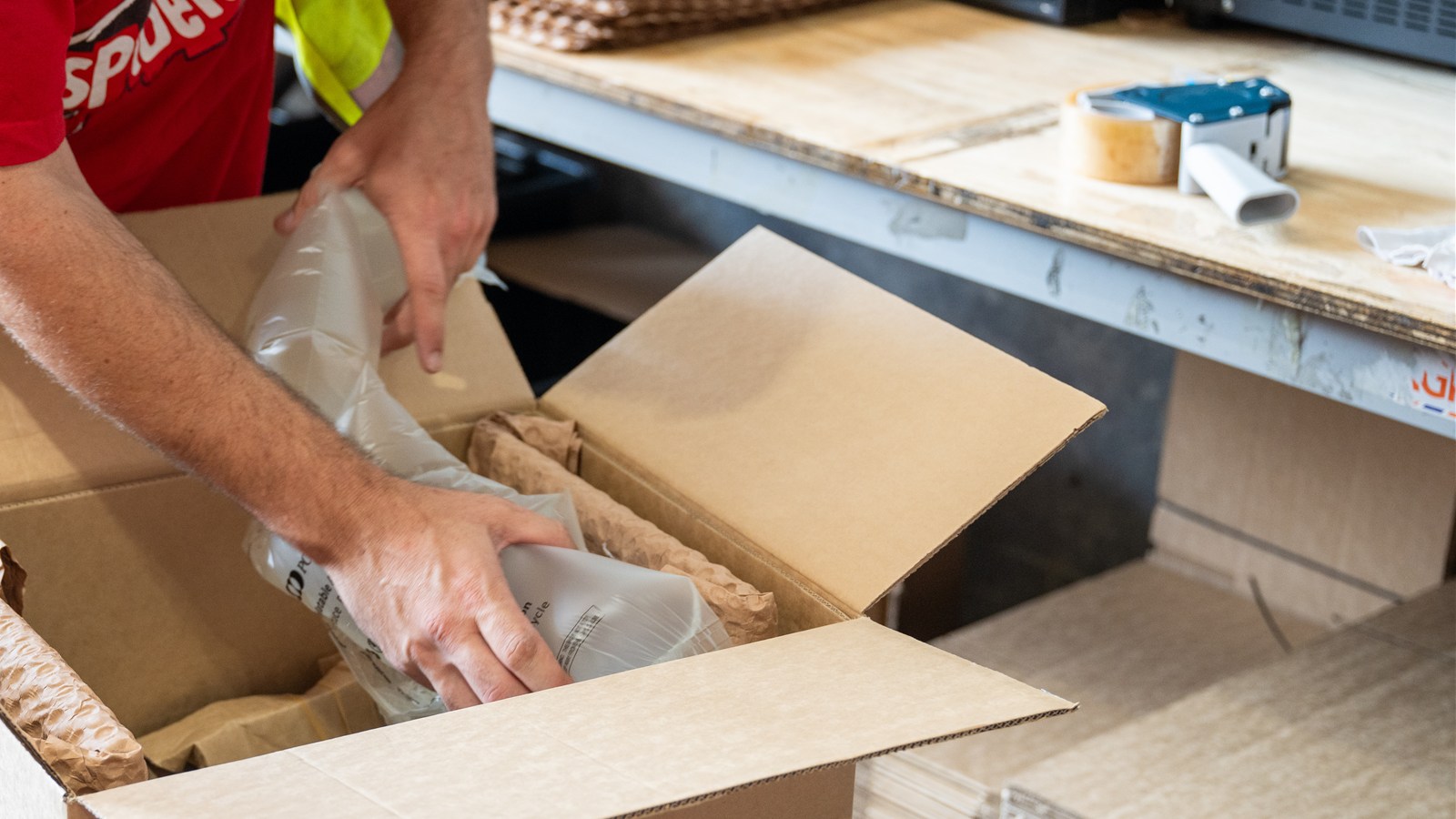 Hands placing protective packing material inside an open cardboard box.